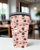 A Halloween-themed cup with a pink background and various ghost and spider motifs, including bats, skulls, and pumpkins.