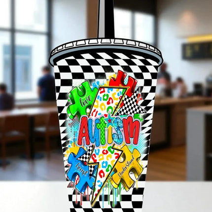 A colorful and vibrant cupcake cup with the word "Autism" prominently displayed on it, surrounded by various puzzle pieces and checkered patterns.
