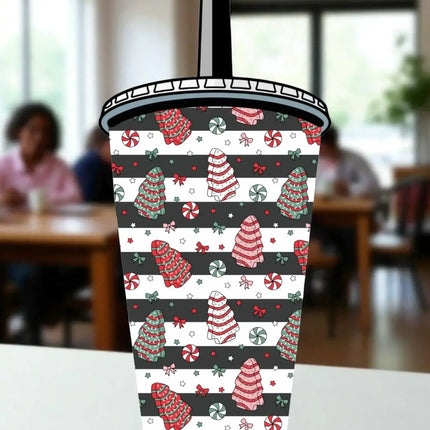 A colorful, patterned cup with Christmas-themed designs, including trees, candy canes, and other festive elements, is displayed on a table.
