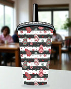 A colorful, patterned cup with Christmas-themed designs, including trees, candy canes, and other festive elements, is displayed on a table.